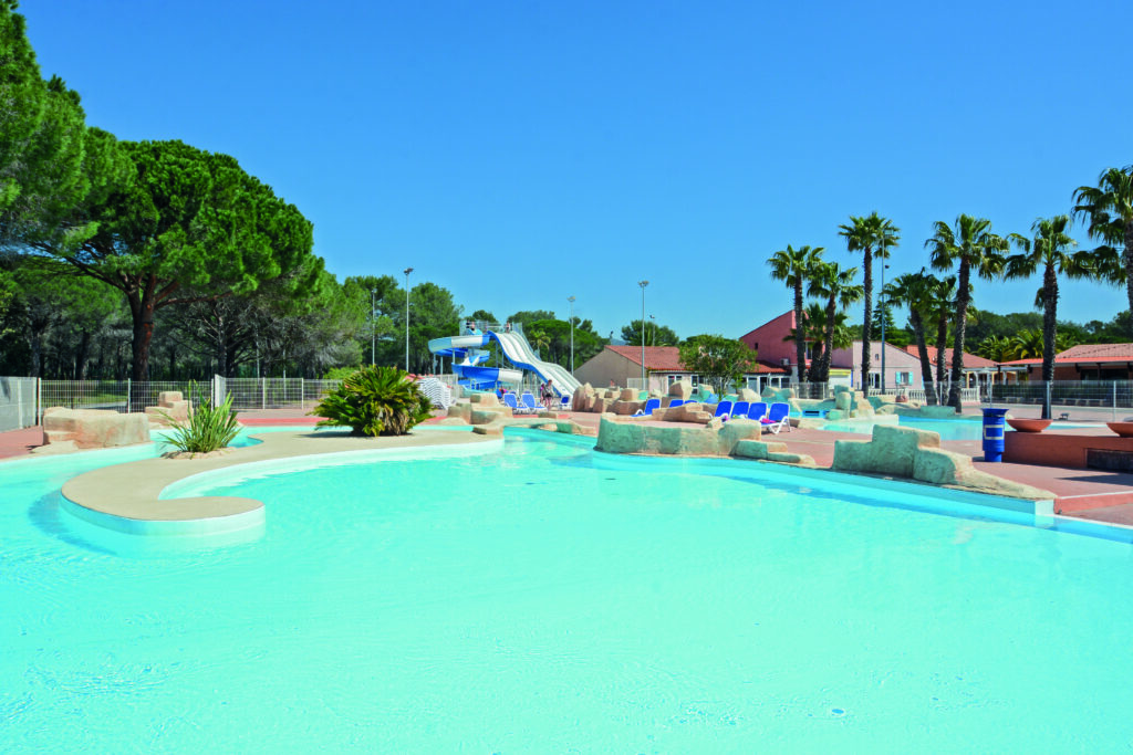 Overview of the Oasis Village water park: lagoon with rocks, palm trees and water slides in the background