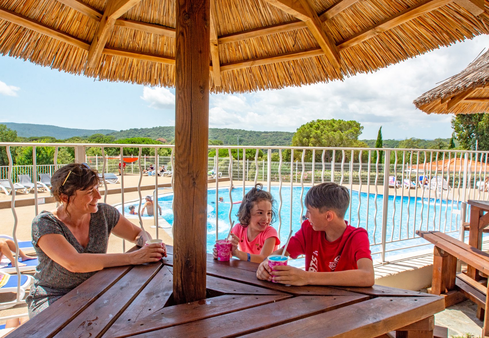 Famille attablée à l'abri sous la paillote, face à la piscine