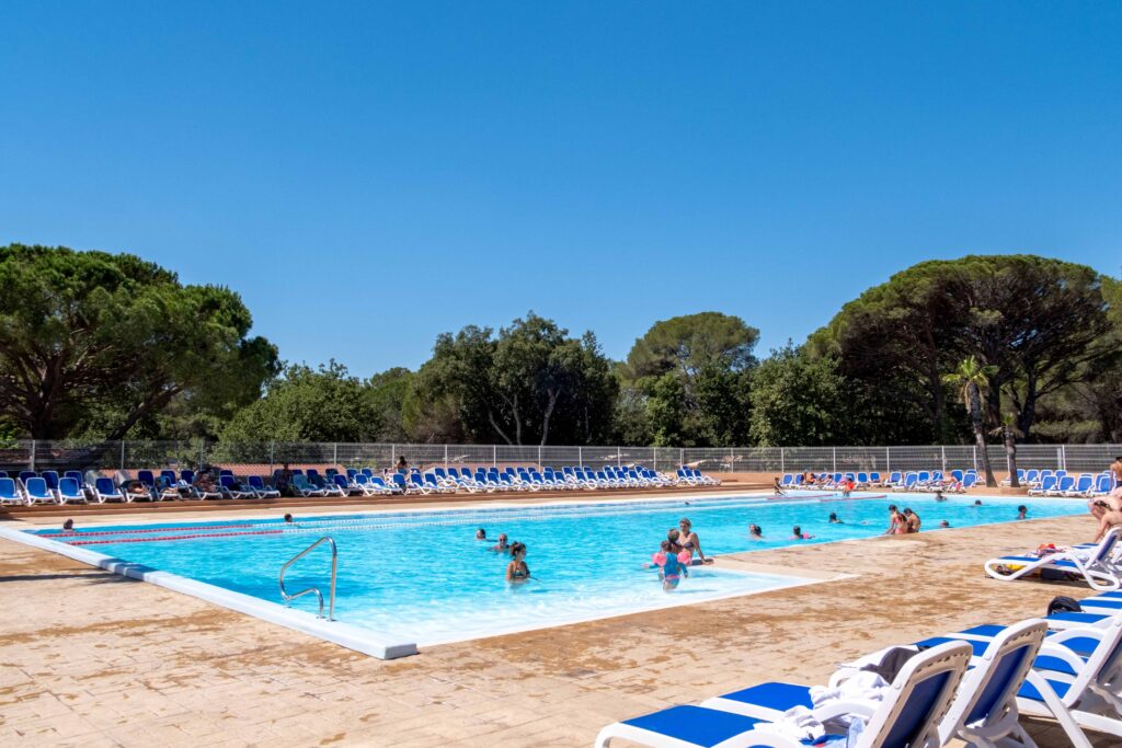 Large outdoor pool in the Oasis Village aquatic area, bordered by sun loungers and umbrella pines